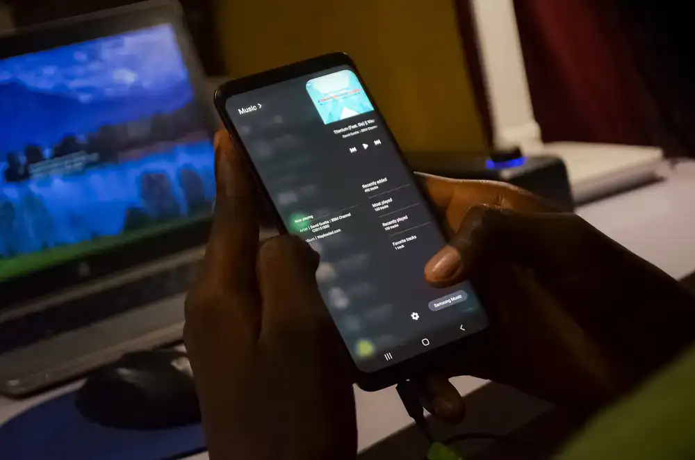 Player holding a mobile device showing an epic fantasy RPG battle